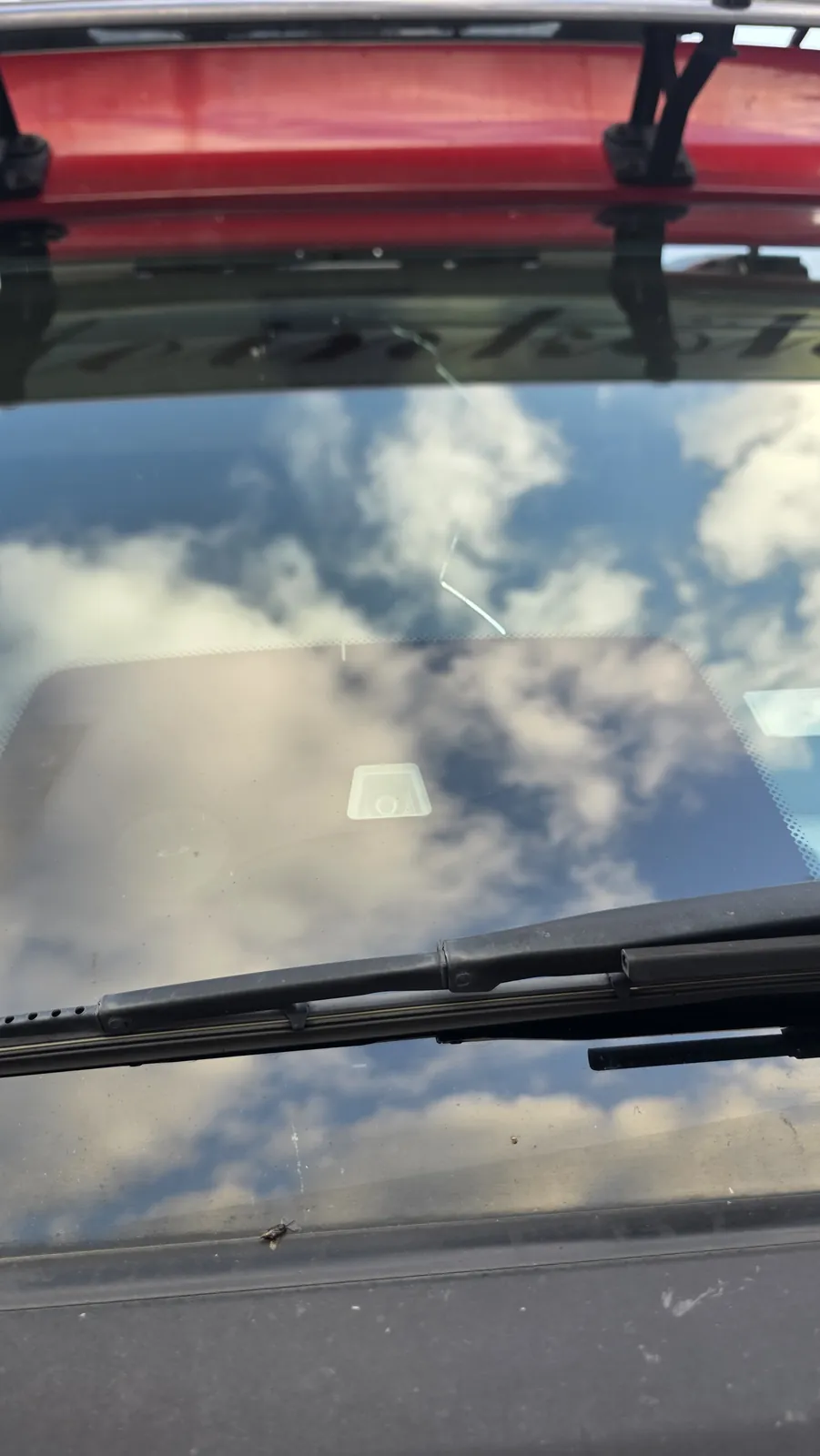 Kleiner Riss im oberen Bereich einer Frontscheibe, im Glas spiegeln sich Wolken