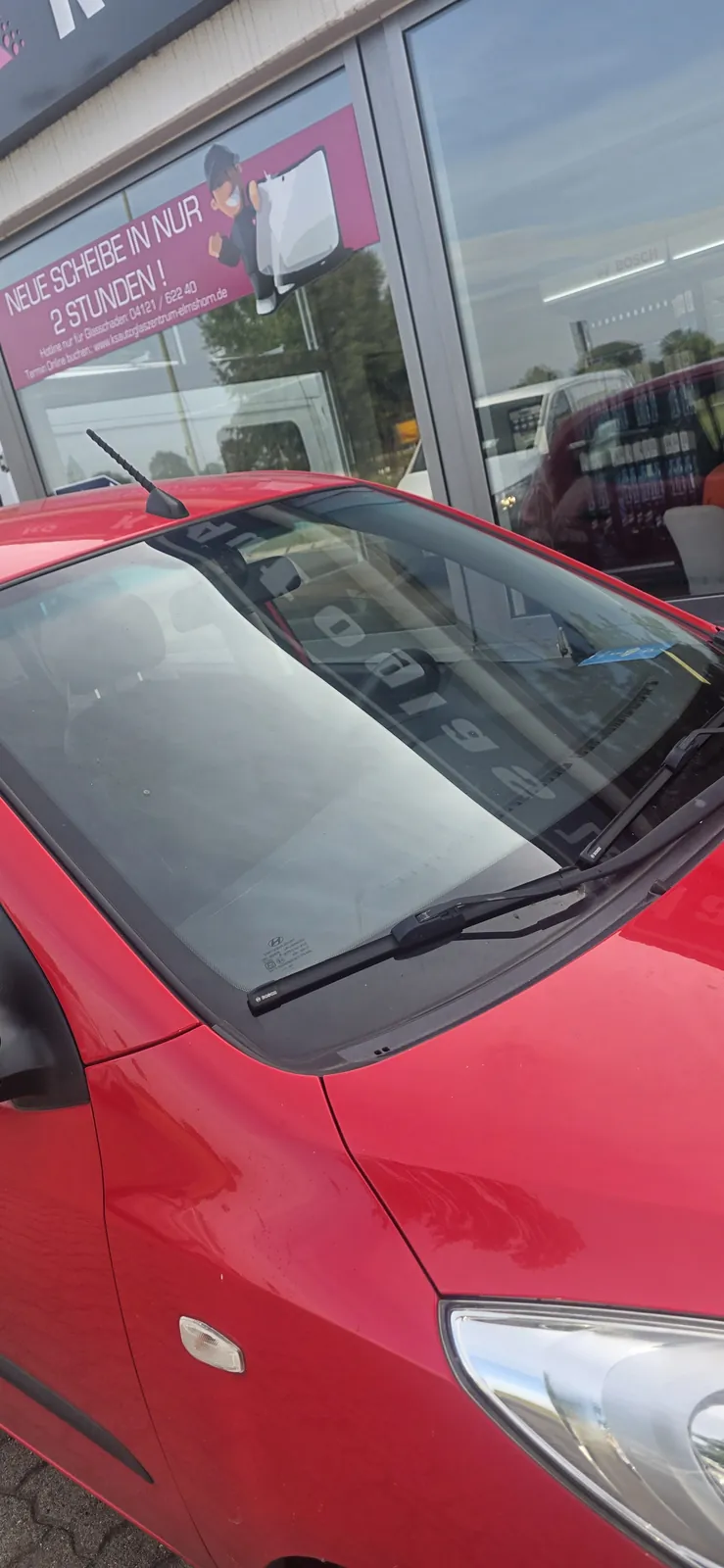 Frontscheibe eines roten Kleinwagens vor dem Schaufenster des KS Autoglas Zentrums