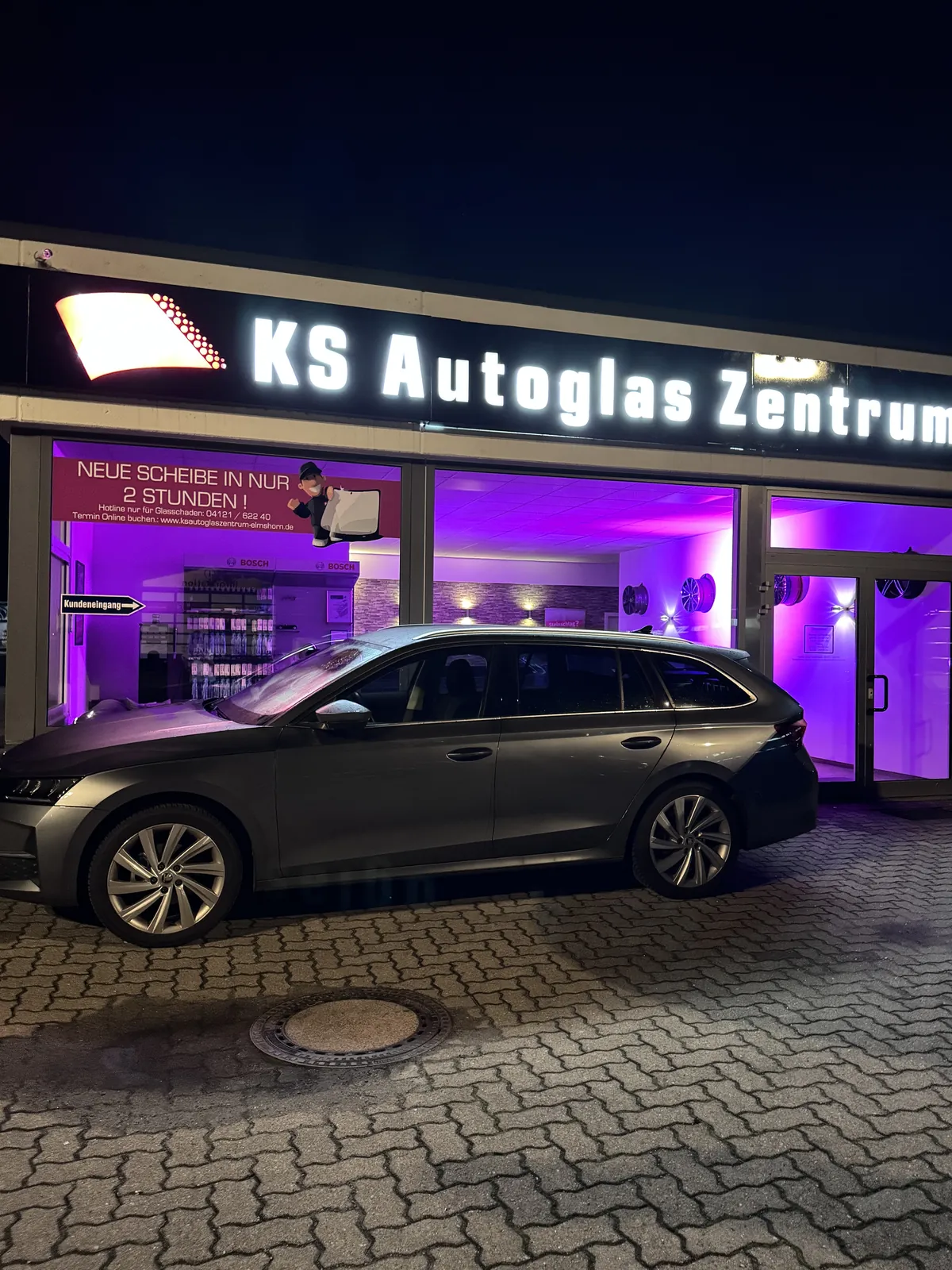 Kombi vor dem beleuchteten KS Autoglas Zentrum in Elmshorn am Abend