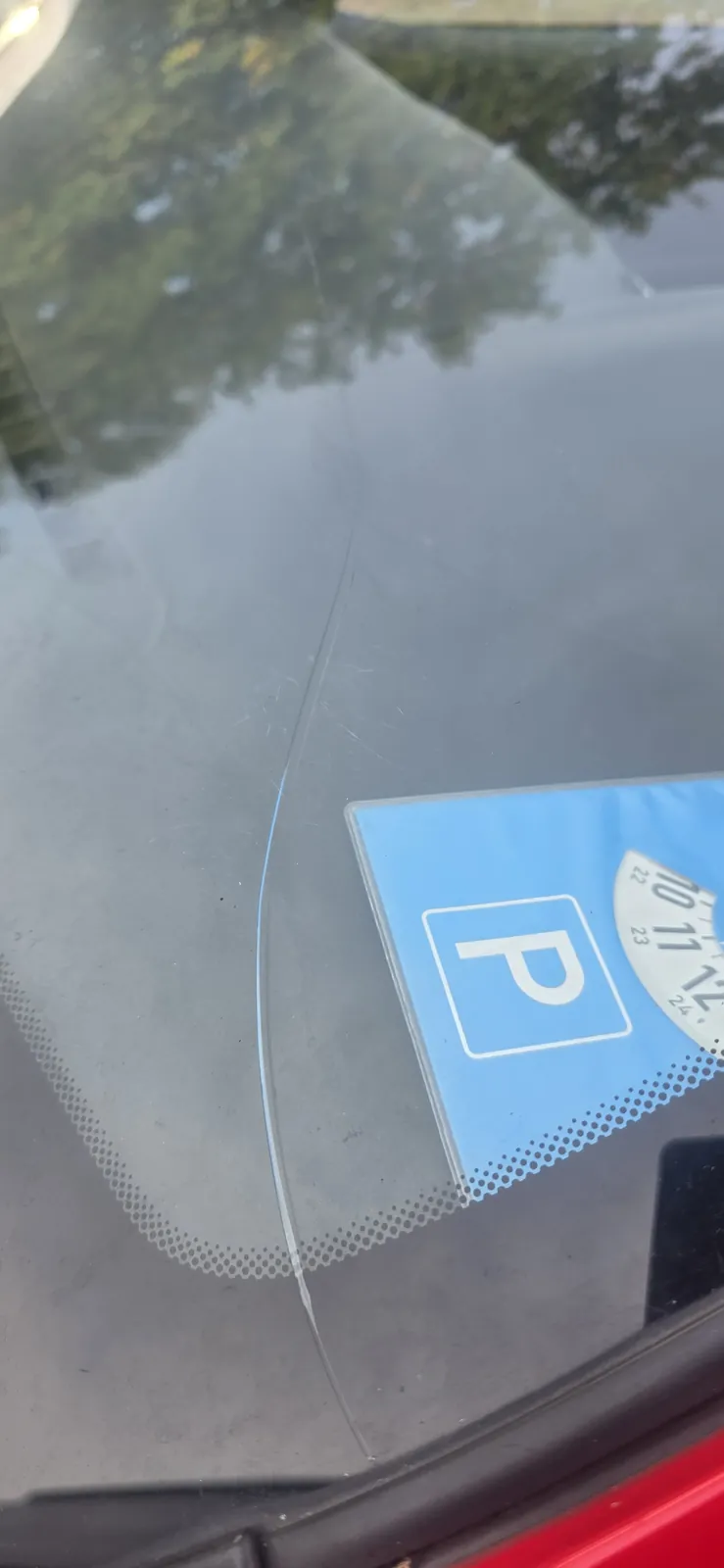 Riss in einer Frontscheibe, dahinter eine Parkscheibe