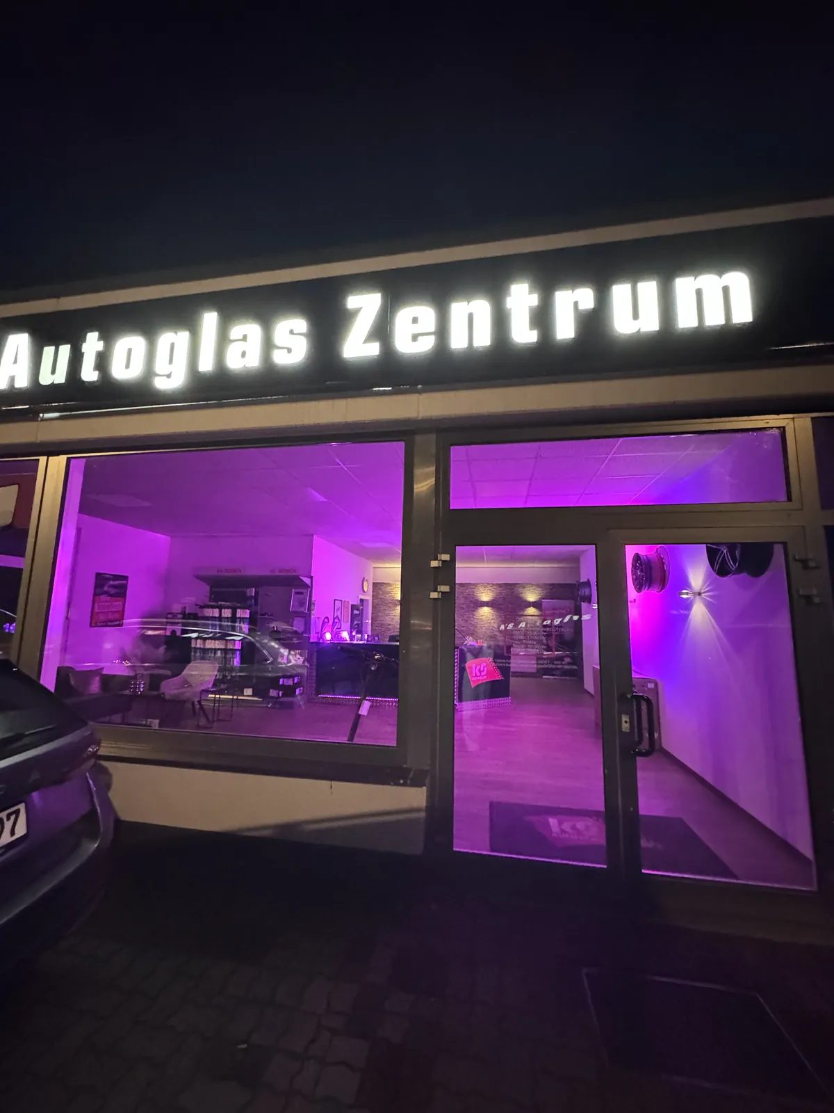 KS Autoglas Zentrum Elmshorn am Abend: beleuchteter Schriftzug und Blick durch die Fenster in den Kundenbereich